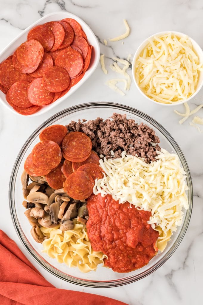 Ground beef, egg noodles, tomato sauce, mushrooms, pepperoni, and mozzarella in a mixing bowl.