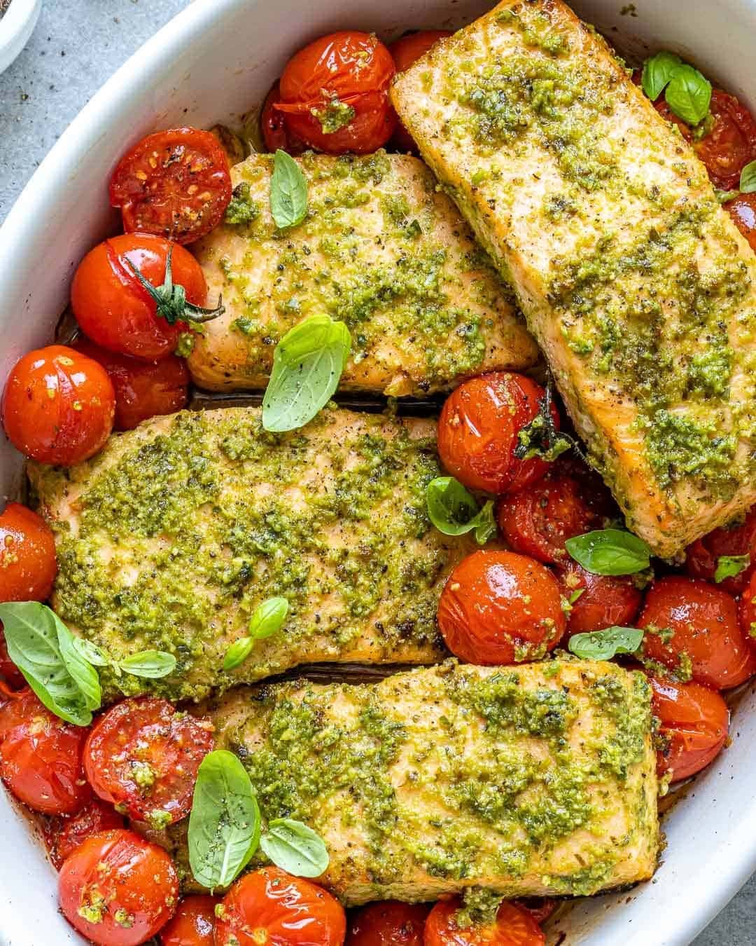 Baked salmon with pesto sauce and cherry tomatoes on a casserole dish.