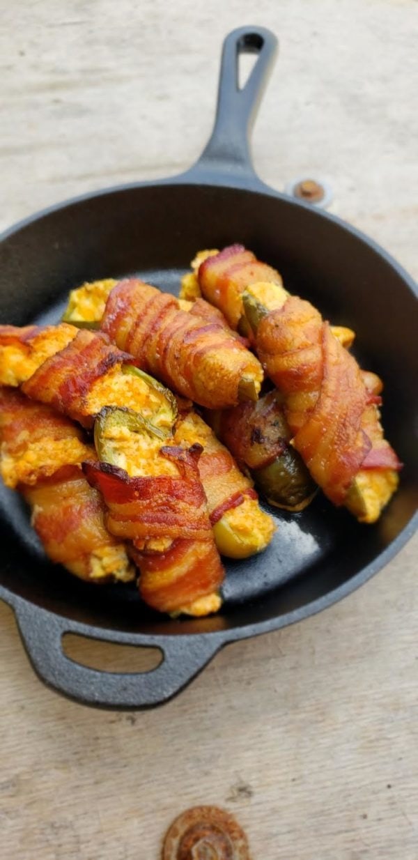 Pickles wrapped with bacon in a cast iron skillet.