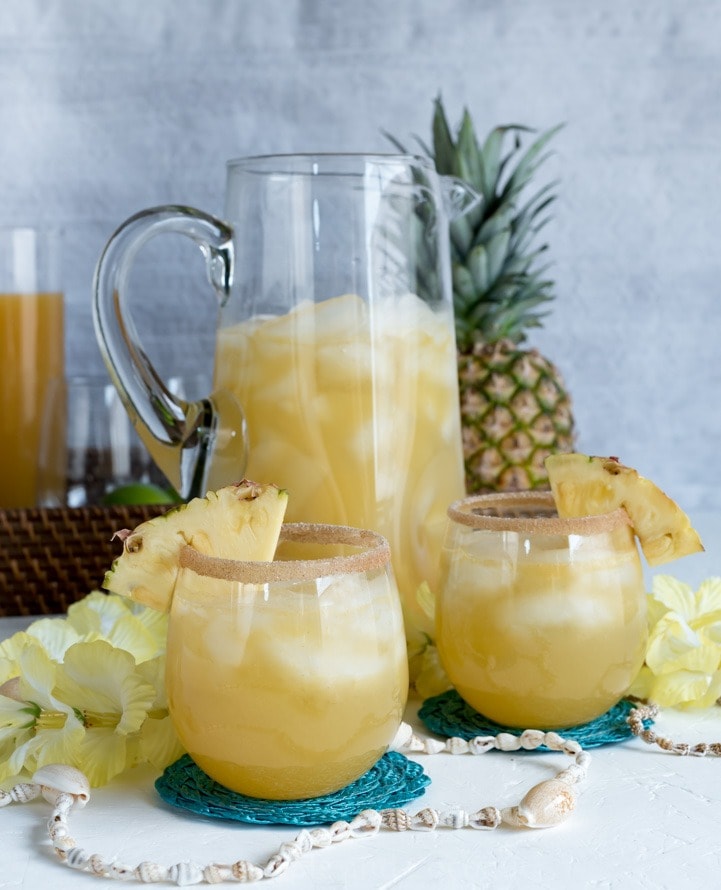 Pineapple punch with chunks on a pitcher and spices-rimmed glasses.