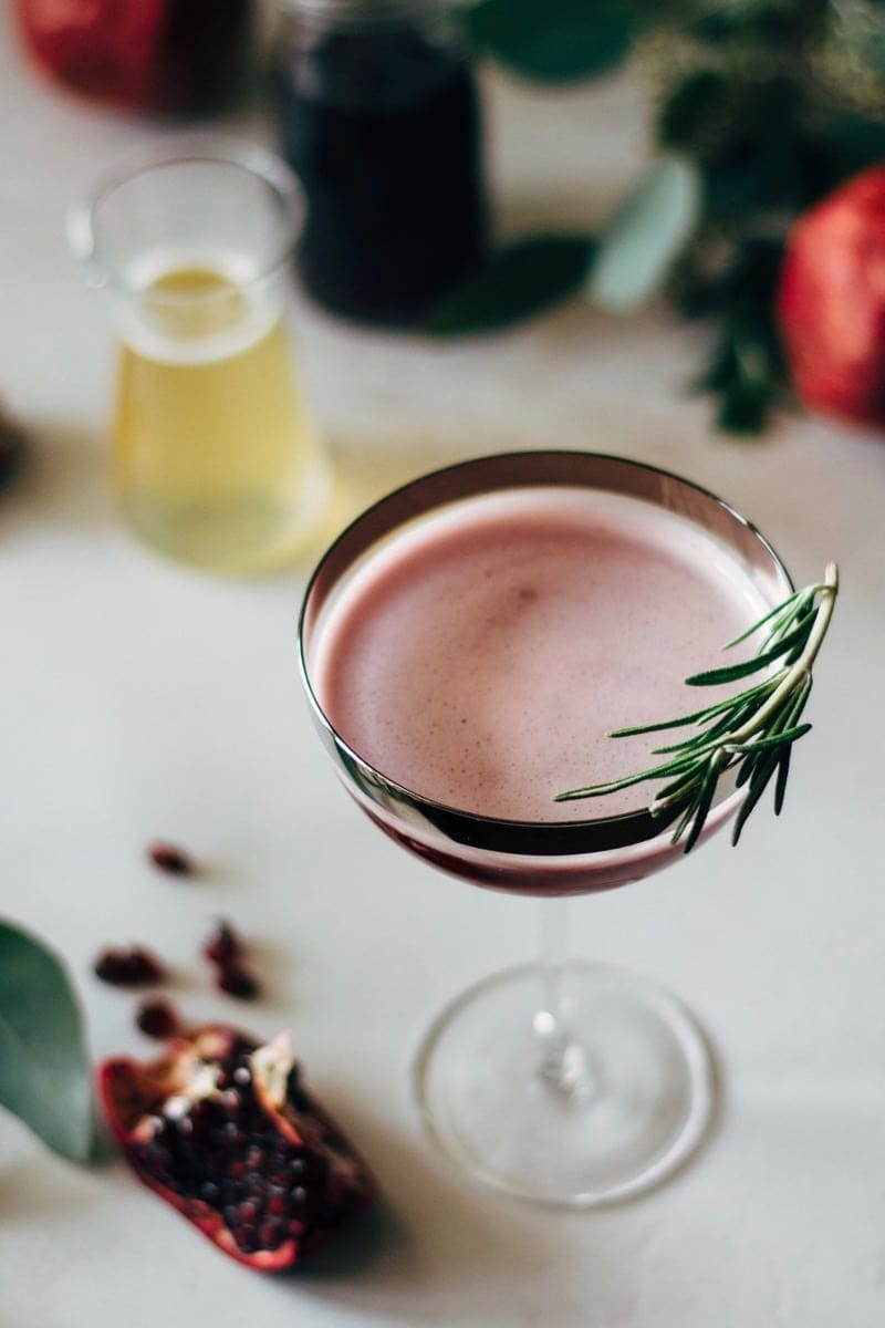 Pomegranate martini with rosemary honey syrup on a cocktail glass.