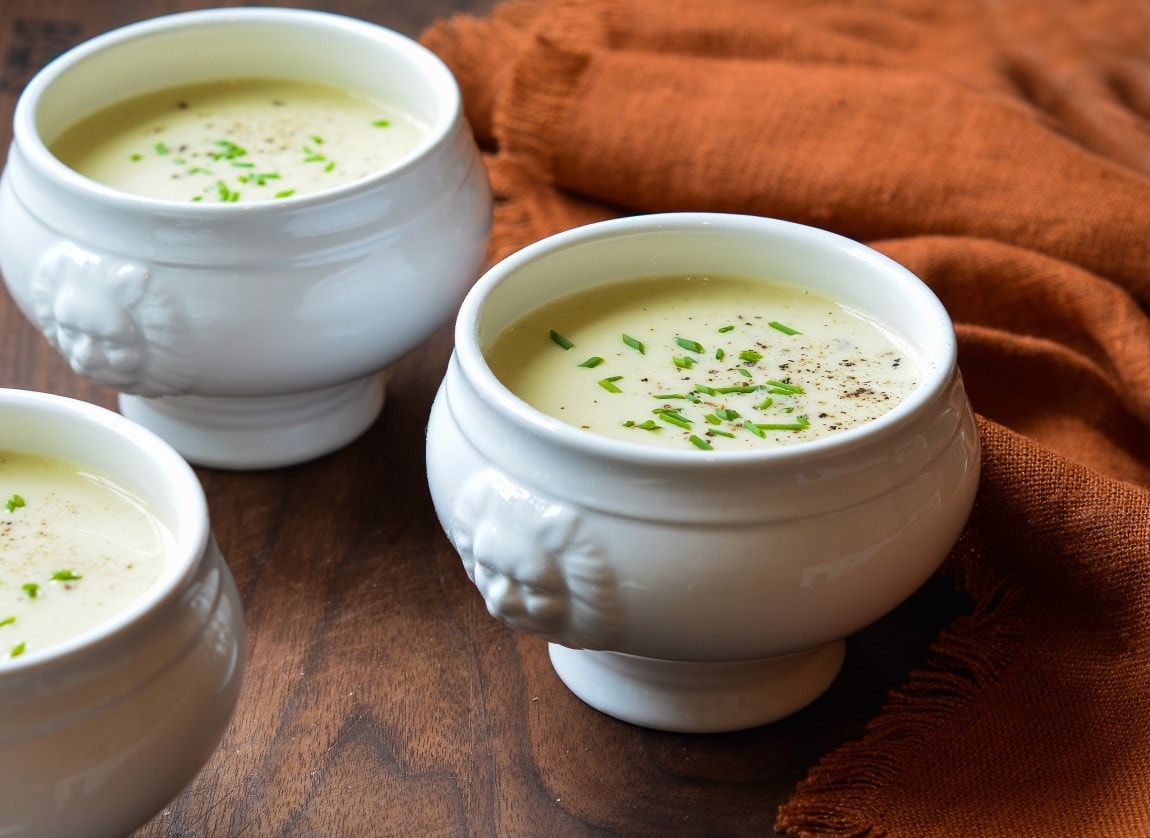 Potato soup garnished with leeks served on a uniquely shaped white ceramic bowls.