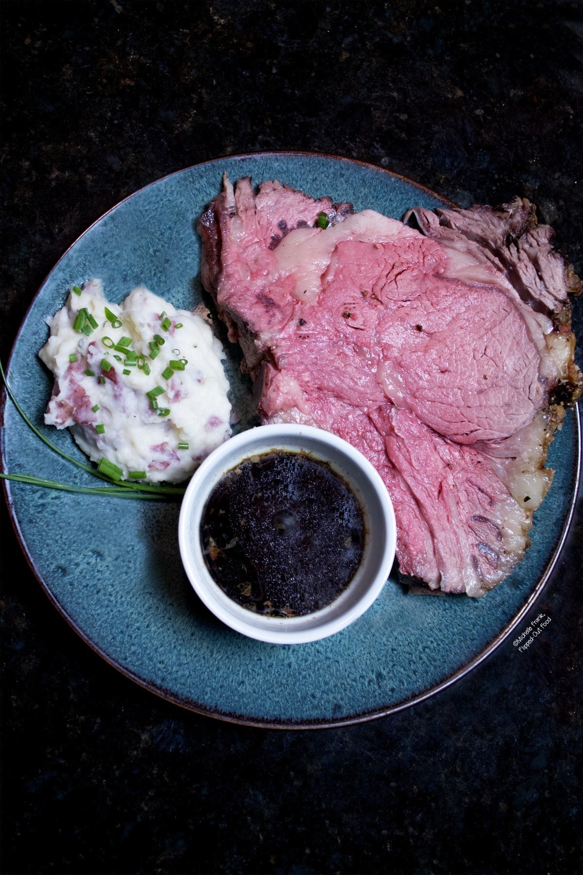 A serving of a slice of roast prime rib on a blue plate with dipping sauce, 