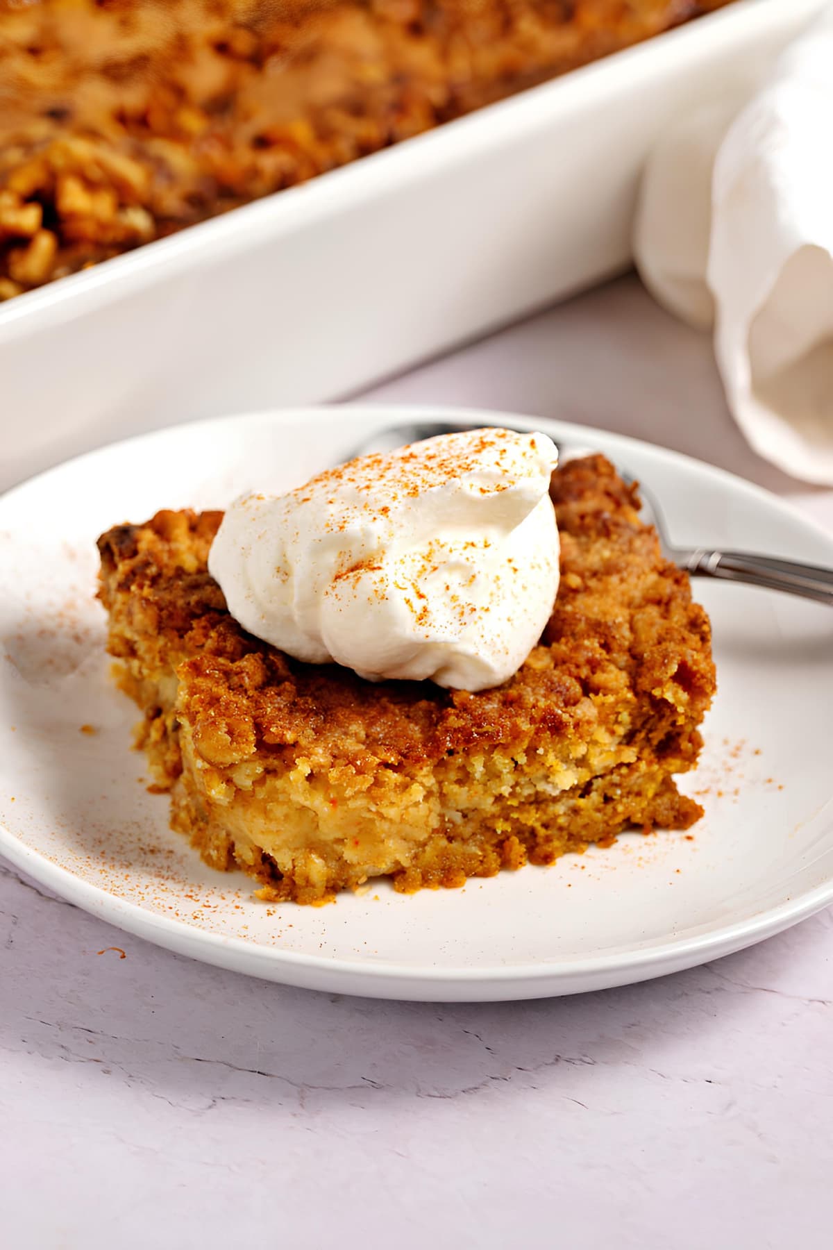 Slice of pumpkin dessert topped with a whipped cream. 
