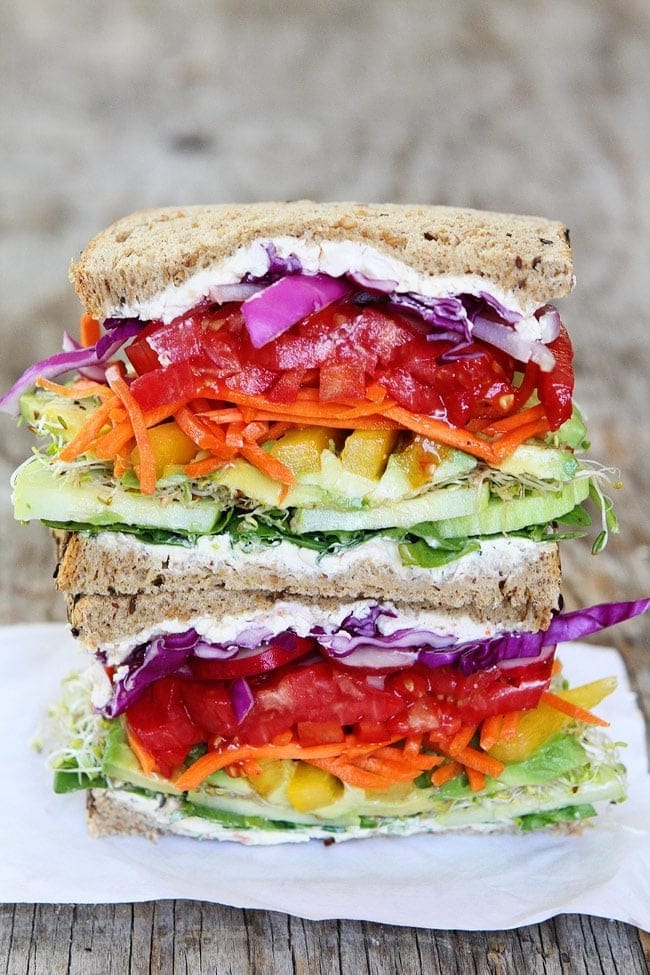 Sliced sandwich with  arugula, cucumber, avocado, sprouts, yellow pepper, carrot sticks, red peppers, tomatoes, radishes, red onion, and purple cabbage filling. 
