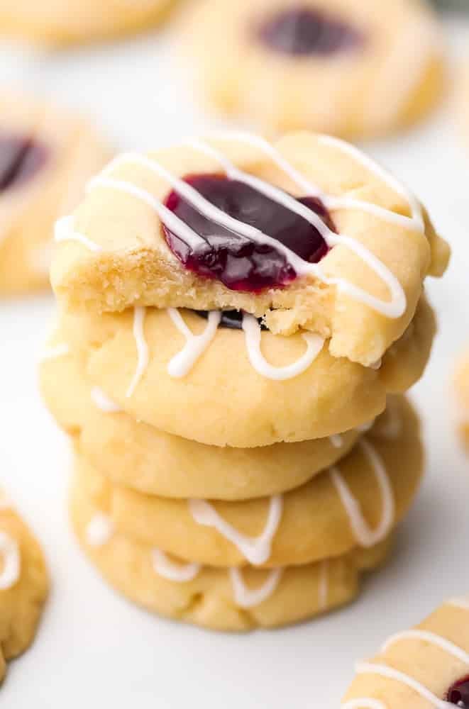 Stacked raspberry almond thumbprint cookies drizzled with white sugar glaze on top. 