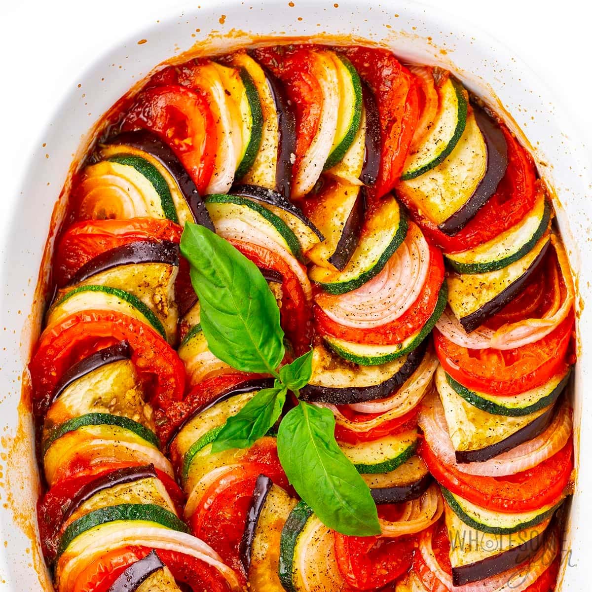 Thinly sliced eggplant, zucchini, and squash with tomato sauce on a pan. 