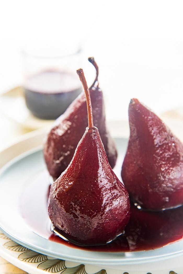 Three pears covered with red wine served on a plate.