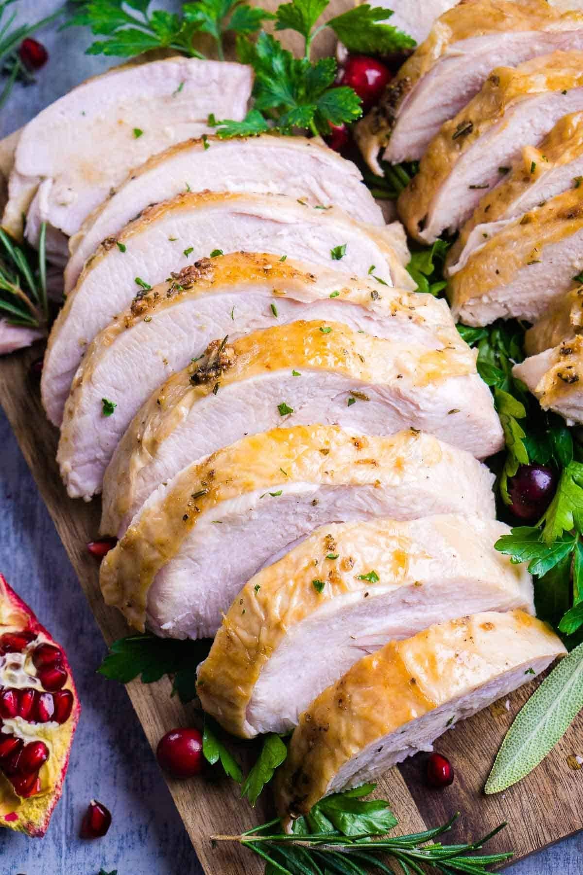 Sliced roasted turkey breast served on a wooden board garnished with cranberries and herbs. 