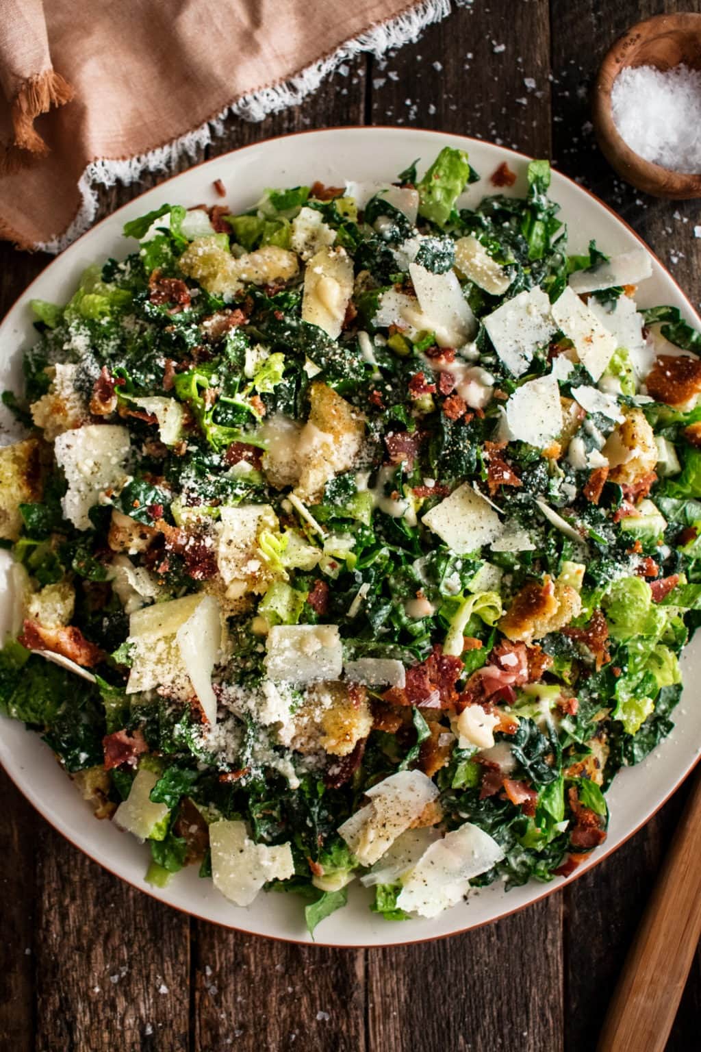 Salad on a white plate made with Thinly sliced romaine and kale, crispy bacon, torn croutons, and lots of parmesan cheese with caesar salad dressing. 