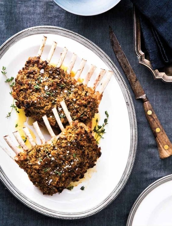 Roasted lamb back on a plate coated with bread crumbs drizzled with sauce.