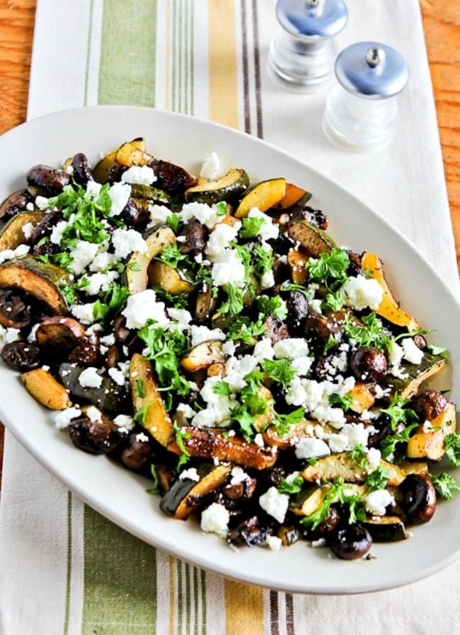 Roasted zucchini and mushrooms on plate topped with goat cheese. 