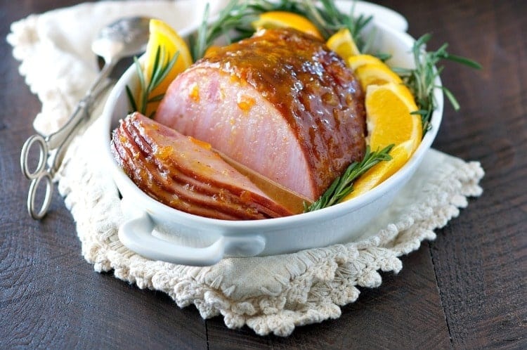 Sliced whole ham with citrus glazed and sliced lemon and rosemary garnish. 
