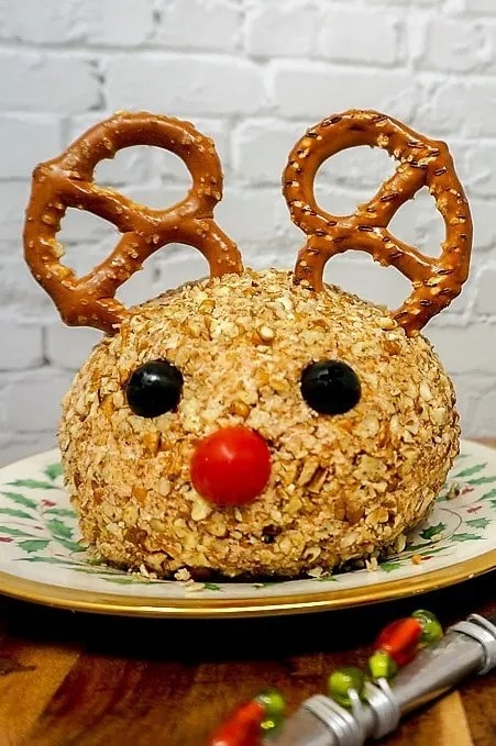 Cheeseball rolled in chopped pecans decorated with olives as eyes, tomato cherries as nose and pretzels as antlers. 