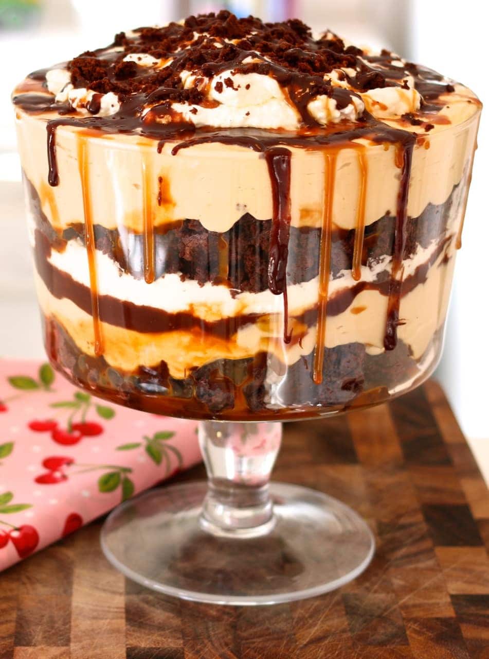 Trifle in a glass bowl made with layers of brownies, cream topped with whipped cream and finish off with drizzle of salted caramel and chocolate syrup on top. 