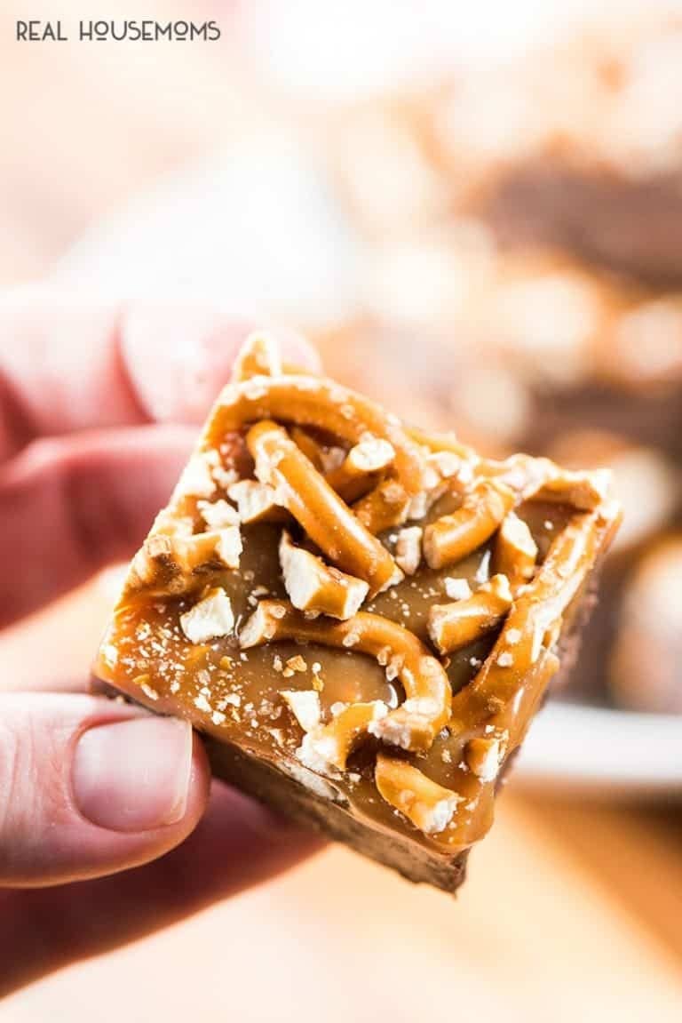 Hand holding a piece of caramel fudge with chopped pretzels on top. 