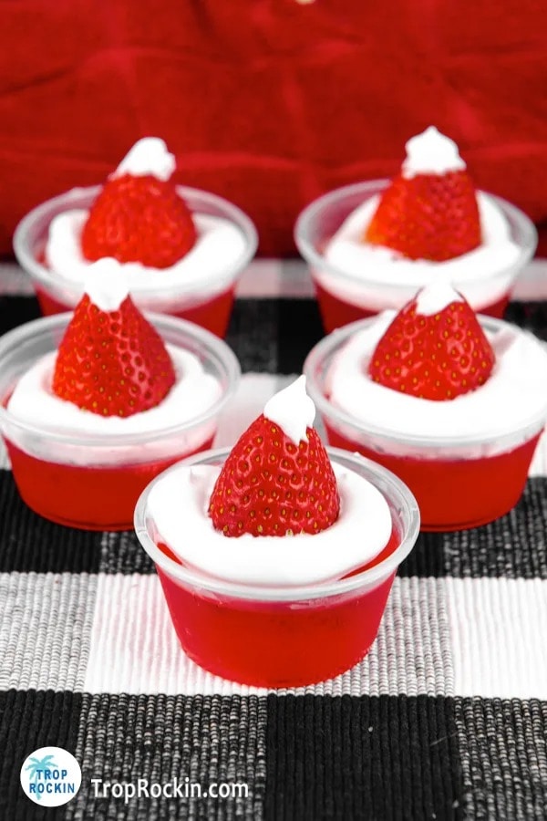 Red Jello shots on plastic cups with strawberry and whipped cream on top. 