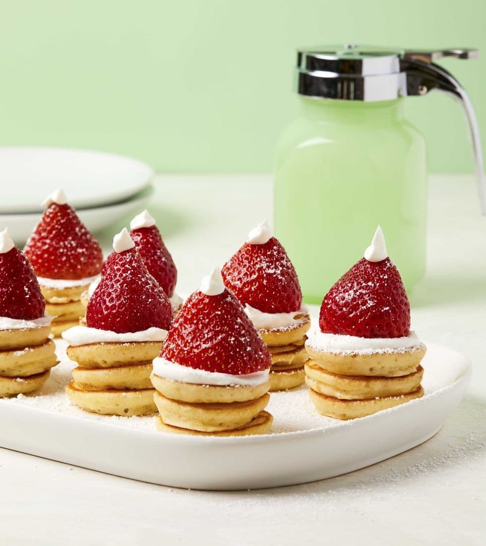 Bunch of mini pancakes decorated with strawberries and whipped cream on top.