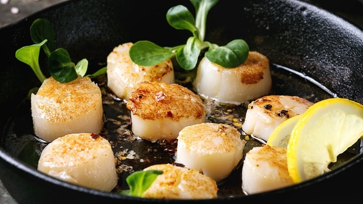 Scallops seared in a cast iron skillet with lemon slices. 