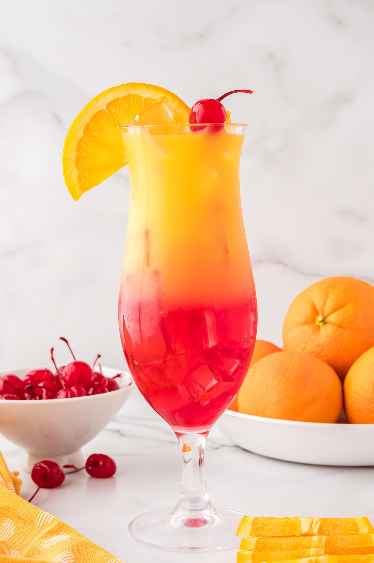 Sex on the beach in a hurricane glass garnished with a maraschino cherry and an orange  slice