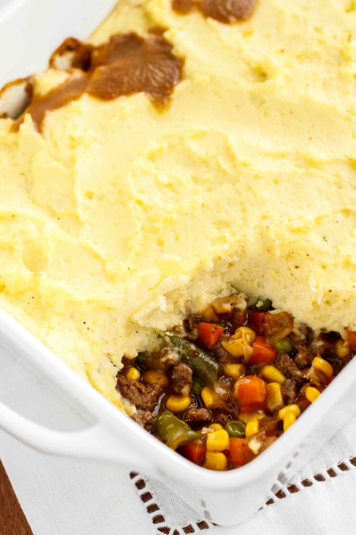Shepherd's pie in a casserole with a portion missing showing corn, green peas, ground beef, and gravy filling.