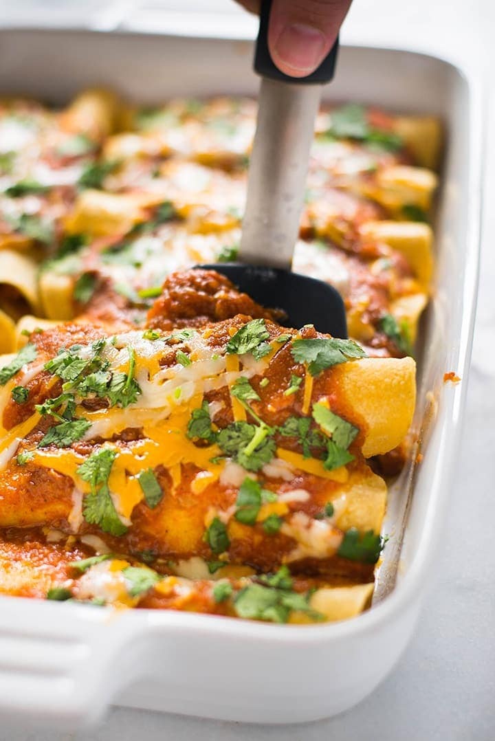 Chicken enchiladas topped with melted cheese, marinara sauce and chopped parsley leaves. 