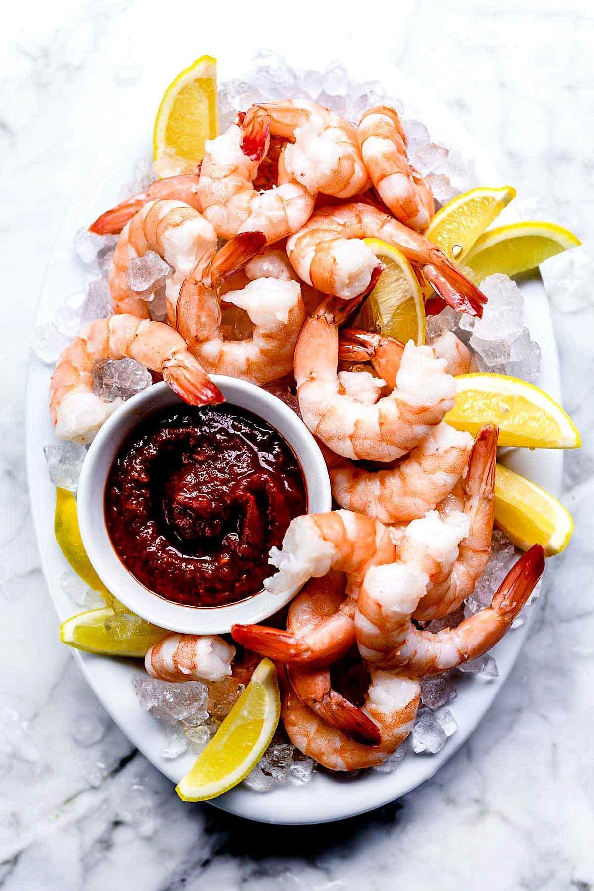 Boiled shrimp with red sauce and sliced lemon on top of ice. 