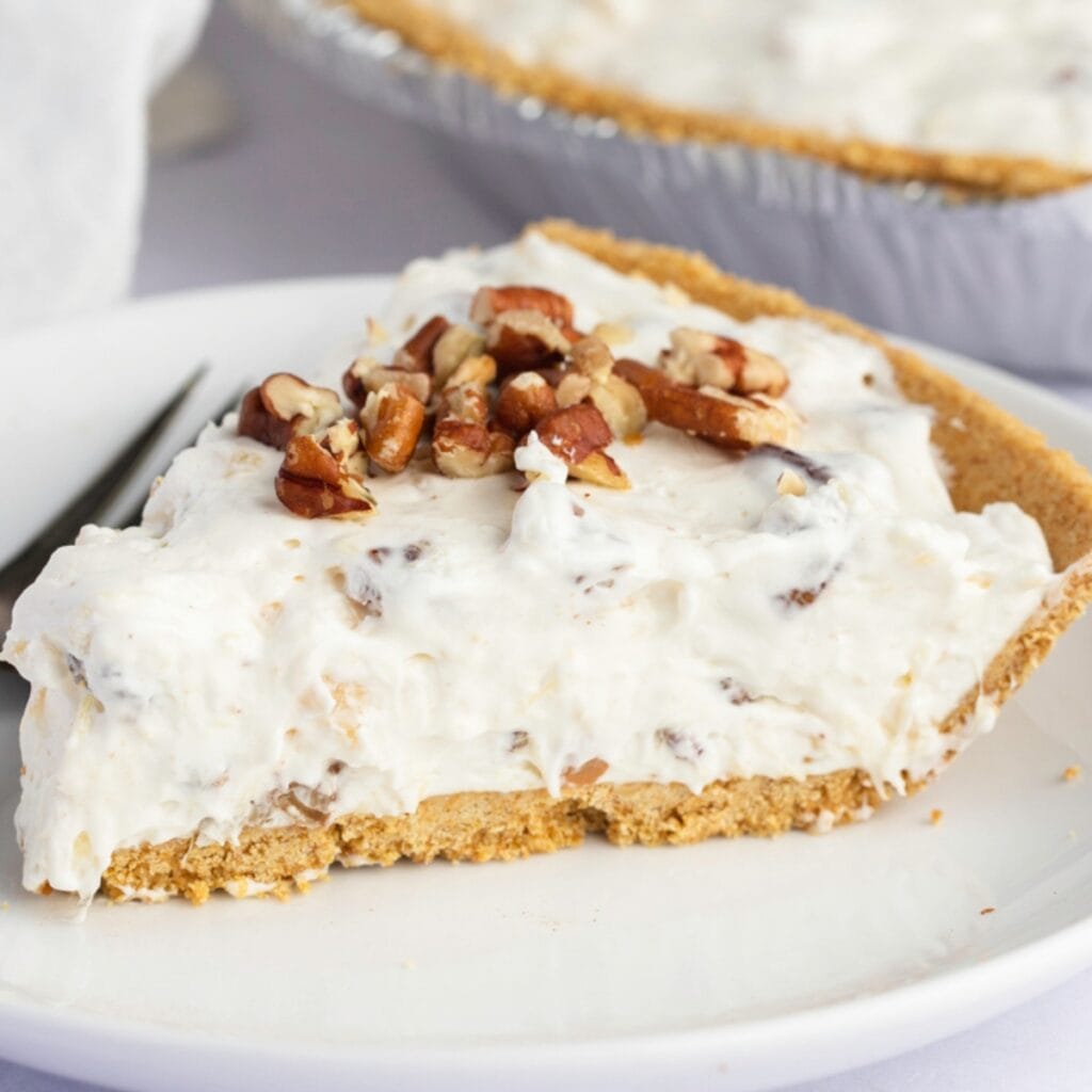 A slice of millionaire pie topped on with chopped pecans served on a white plate. 