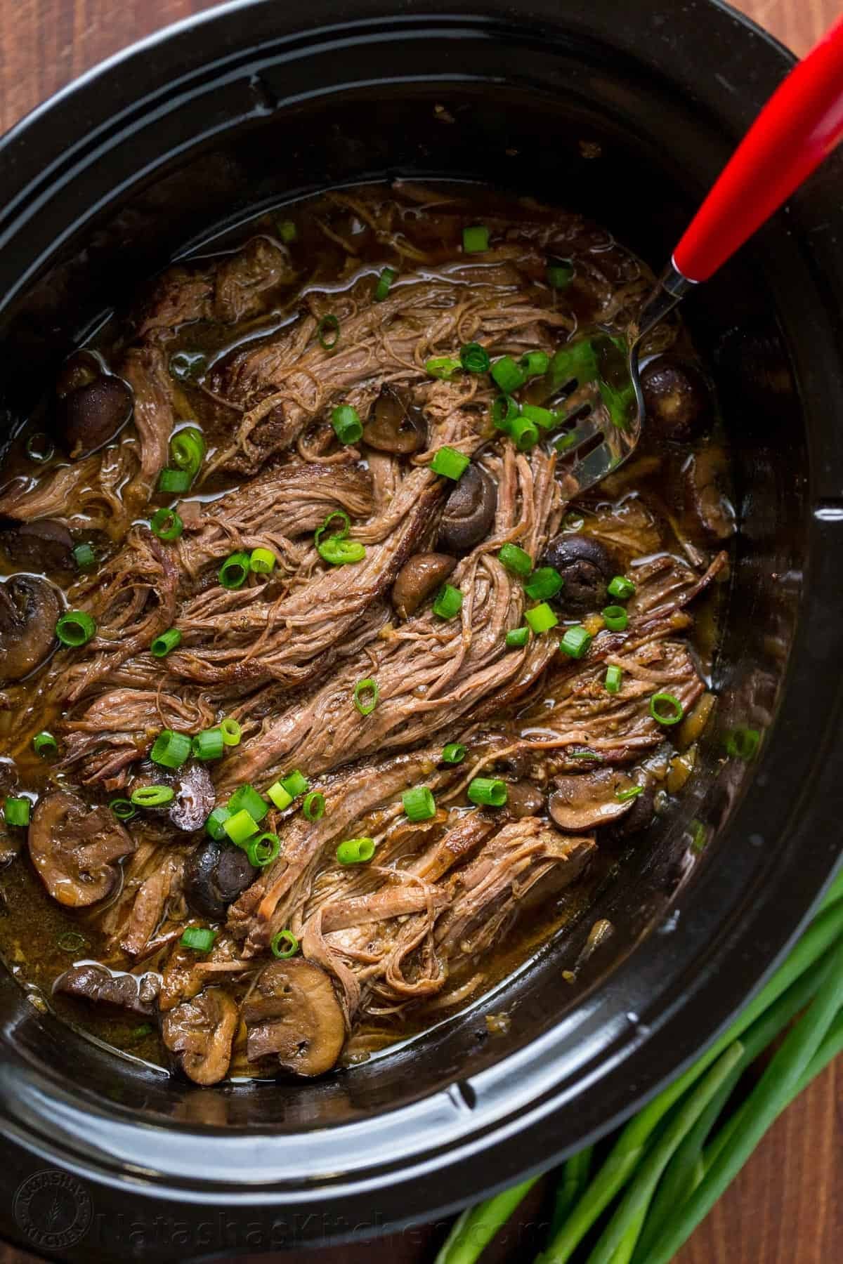 Beef brisket with caramelized onions and mushrooms on a crockpot.