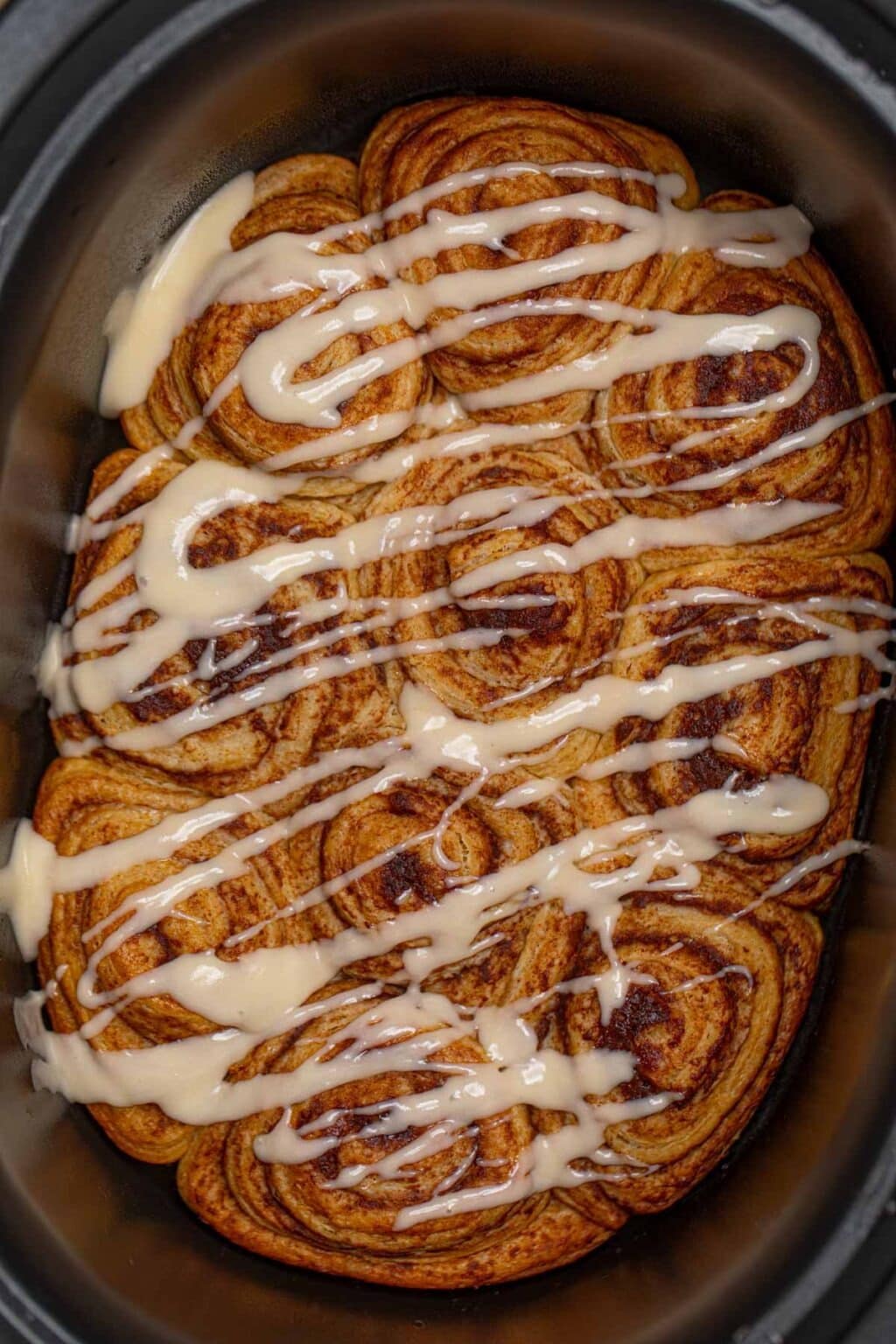 Cinnamon rolls in a crockpot drizzled with white sugar glaze.