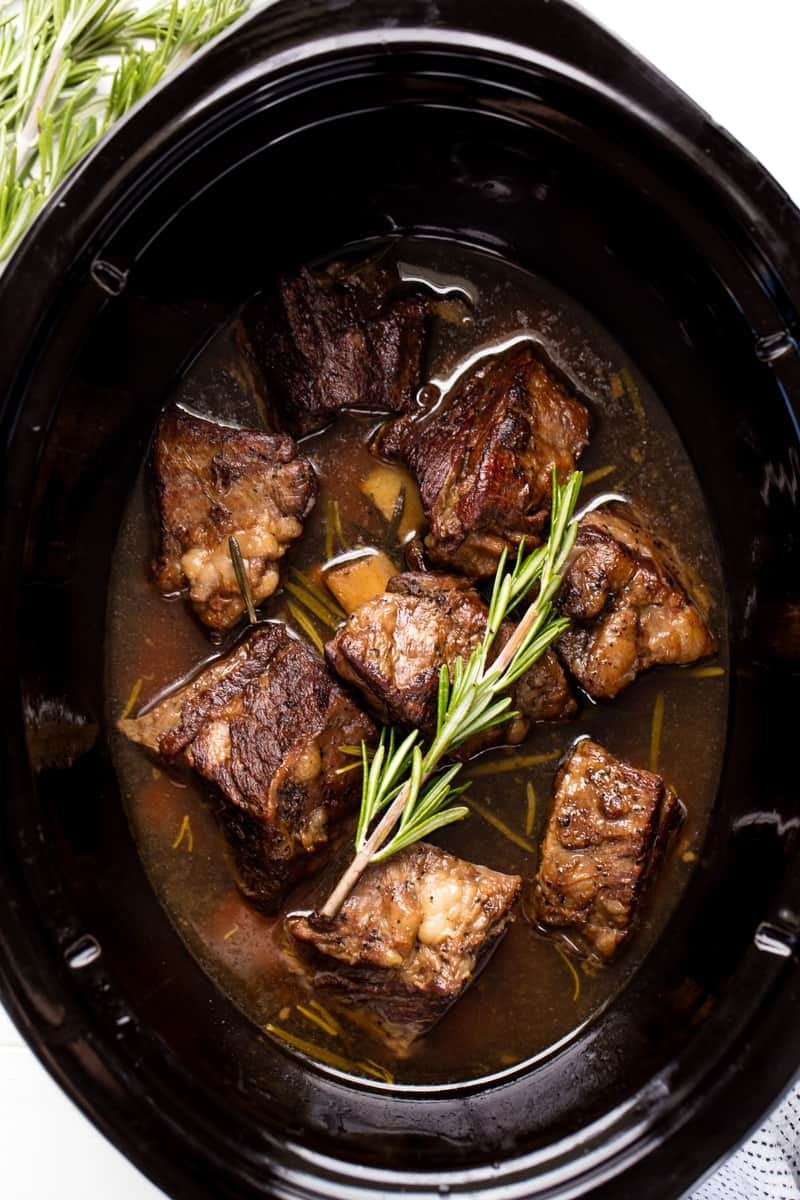 Beef Short Ribs in a slow cooker garnished with rosemary