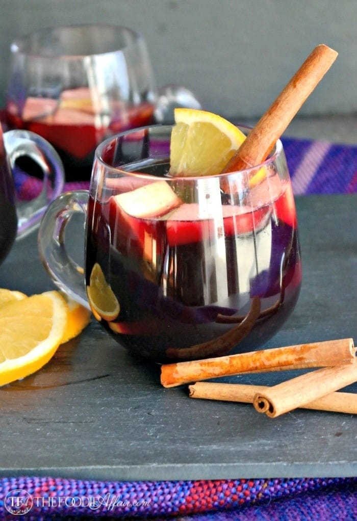 Red sangria on a glass mug garnished with lemon slices, apples and cinnamon stick. 
