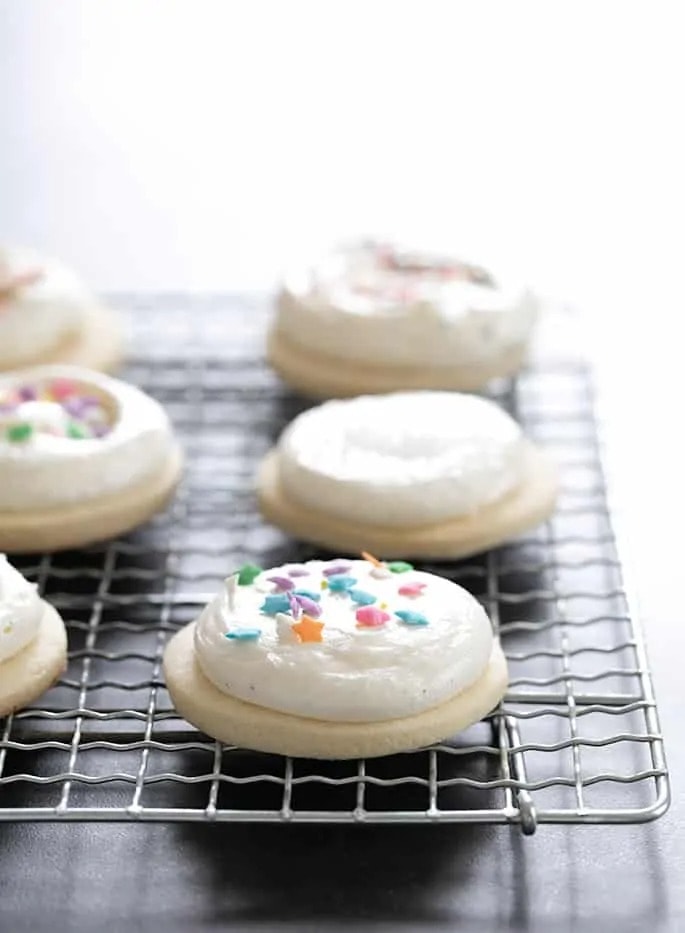 Sugar Cookies topped with frosting with sprinkles on a cooling rack. 