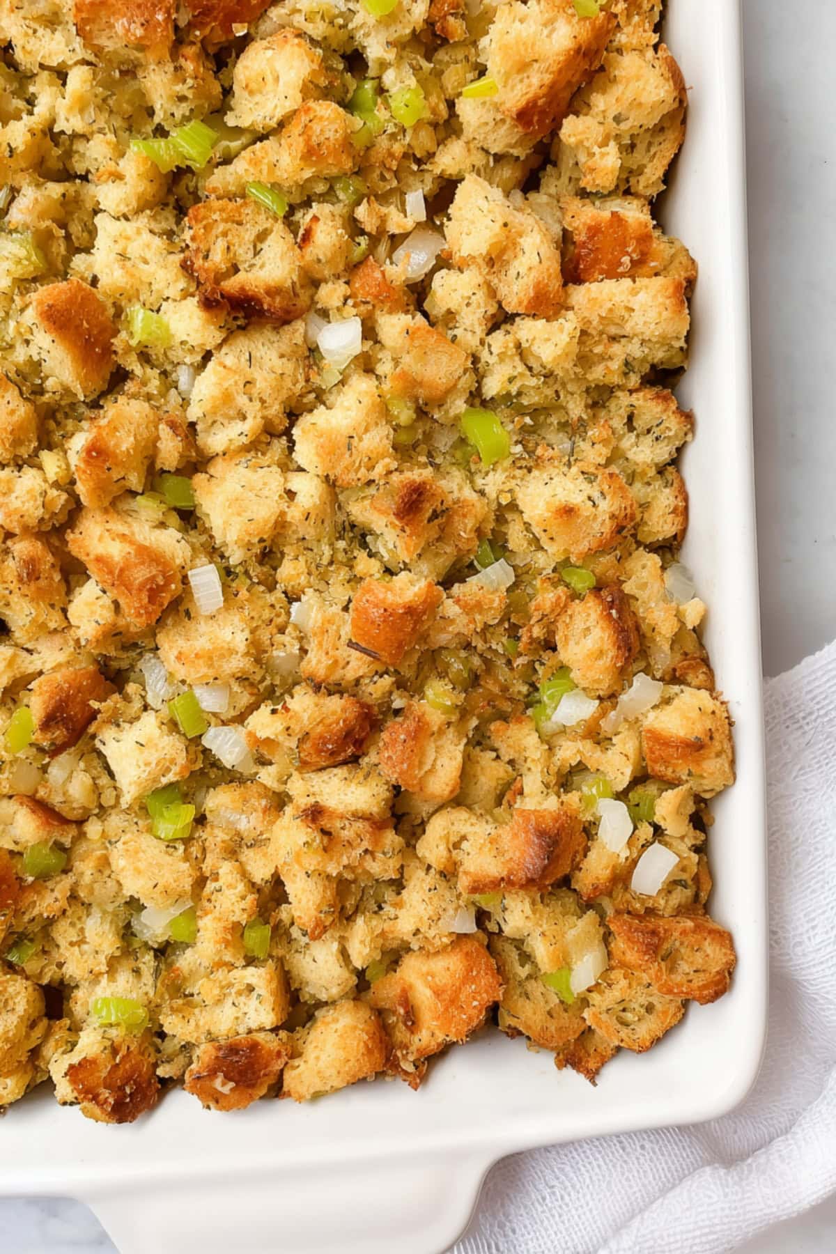 An overhead view of Southern cornbread dressing with white onions and chopped celery in a white baking dish. - 7