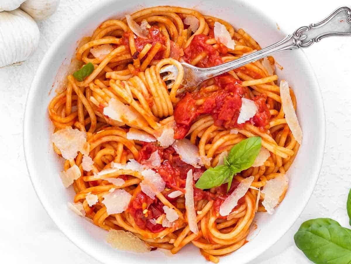 Spaghetti served with crushed tomatoes, cheese and basil leaves on a white bowl.