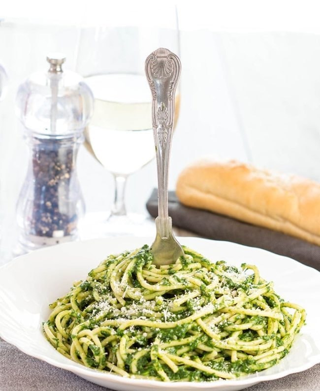 Fork on a serving of spaghetti with spinach sauce garnished with parmesan cheese.