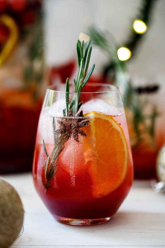 Sparkling sangria on a glass garnished with orange slices and rosemary. 