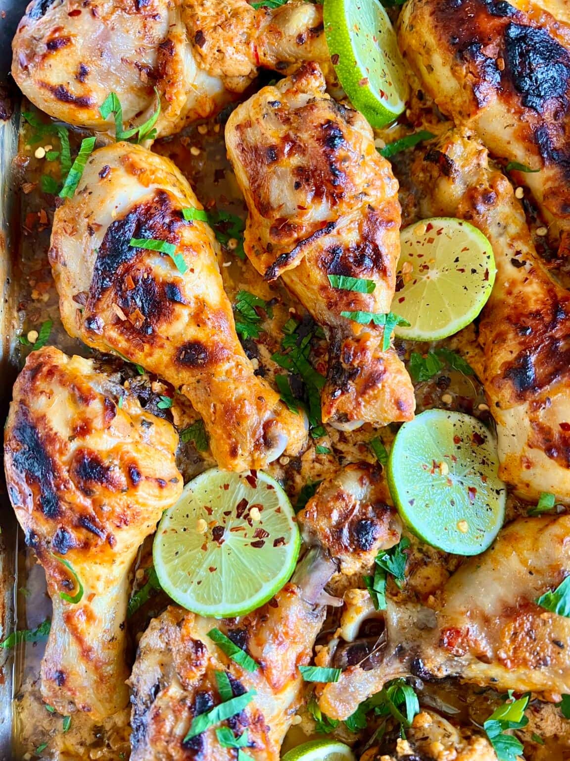 Seasoned chicken legs garnished with lime slices and chopped parsley.
