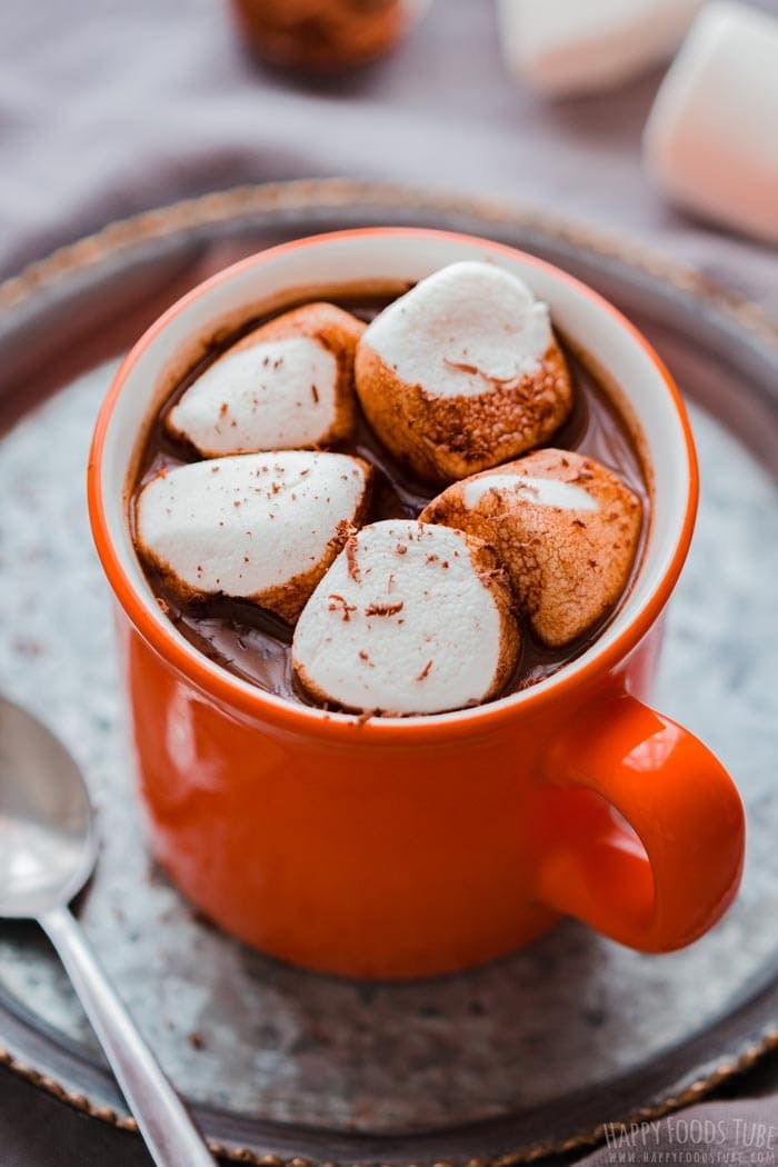 Hot chocolate in orange mug topped with marshmallows. 