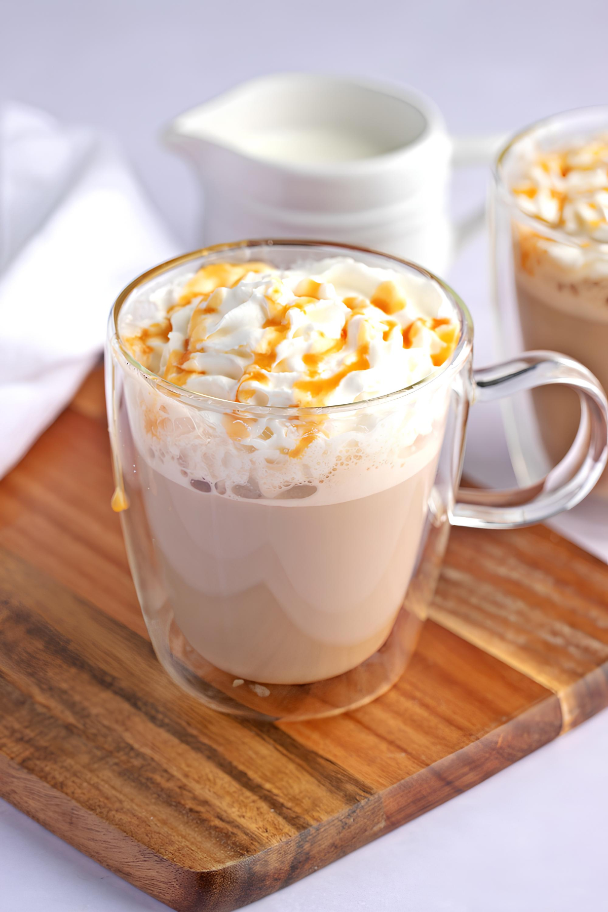 Copycat Starbucks Caramel Macchiato Recipe featuring Glass mug with homemade Starbucks caramel macchiato with whipped cream and drizzle of caramel on top.