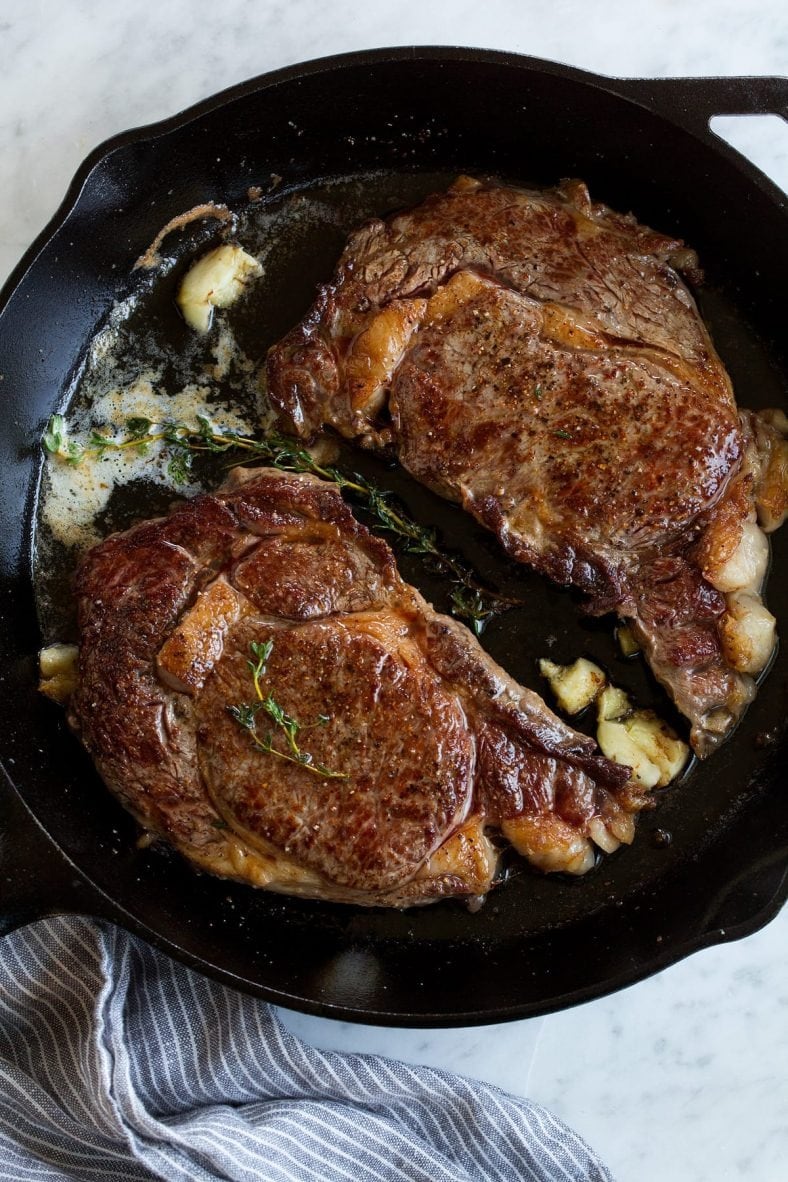 Two sizzling steaks cooked in a skillet on a table with thyme