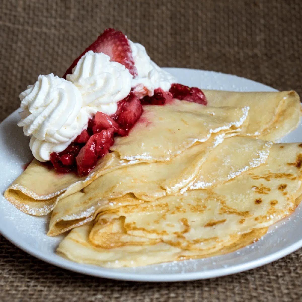 Stack of crepe with strawberries and whipped cream on top served on a plate
