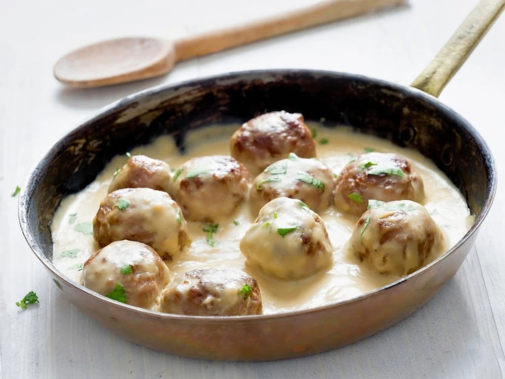 Swedish meatball served with mashed potato on a black plate.