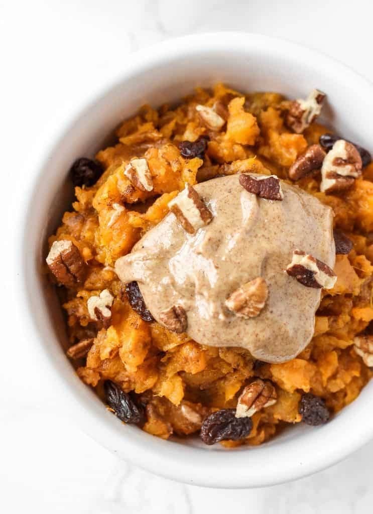 Bowl of mashed sweet potatoes with nuts and peanut butter on top.