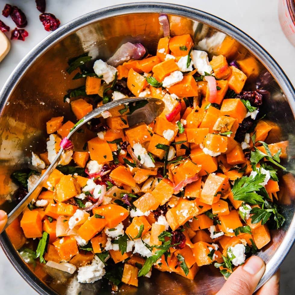 Sweet potato salad with chopped onions, herbs and feta cheese on mixing bowl. 