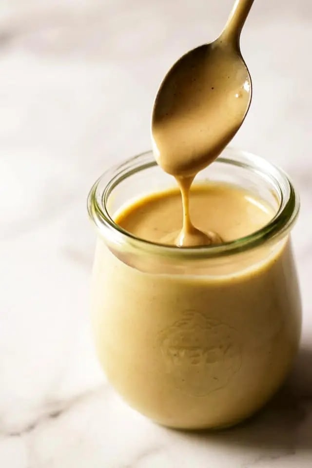 A jar filled with creamy tahini dressing, made from scratch using fresh ingredients.