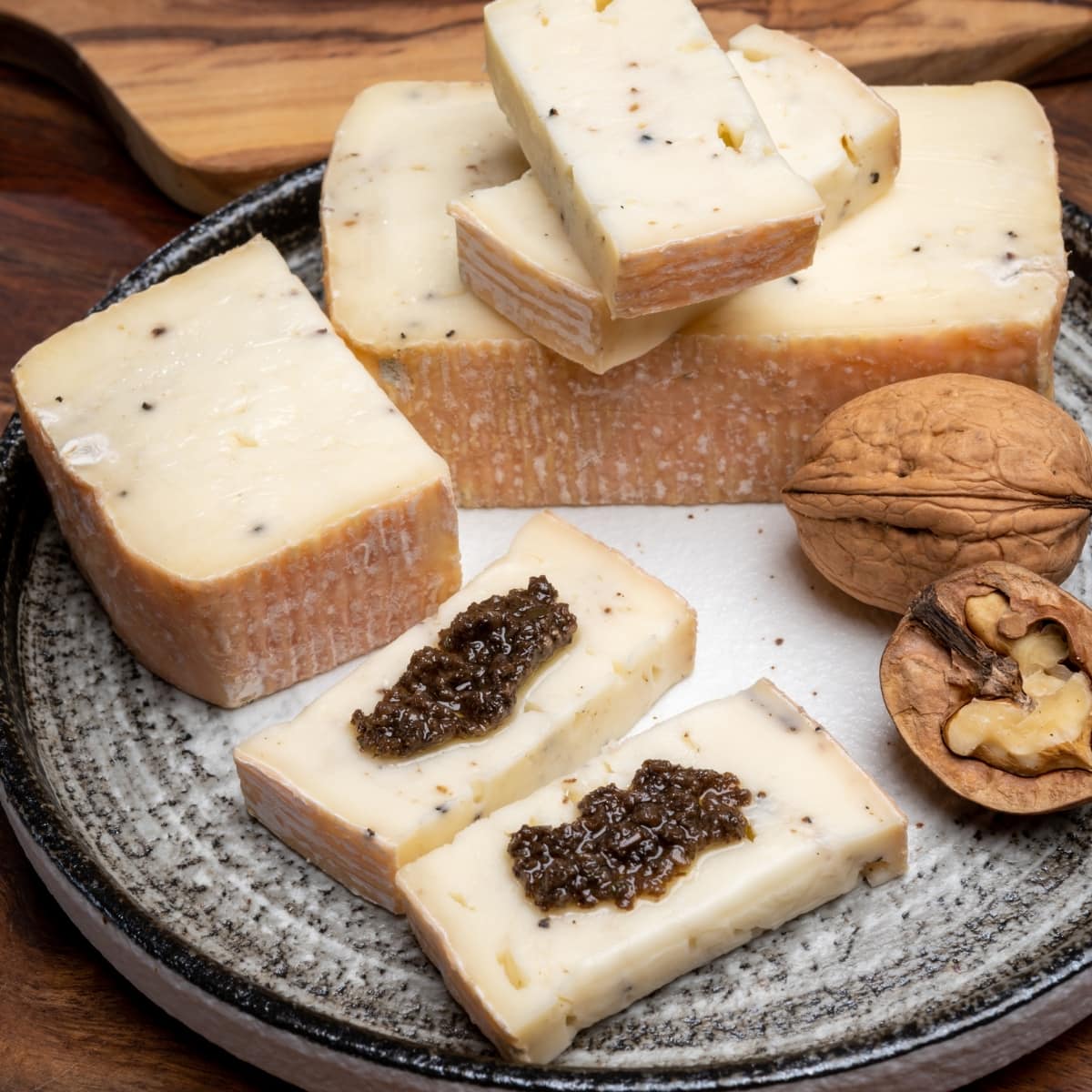 Raw Organic Taleggio Cheese Block and Slices with Walnuts and Tapenade on a Round Cutting Board