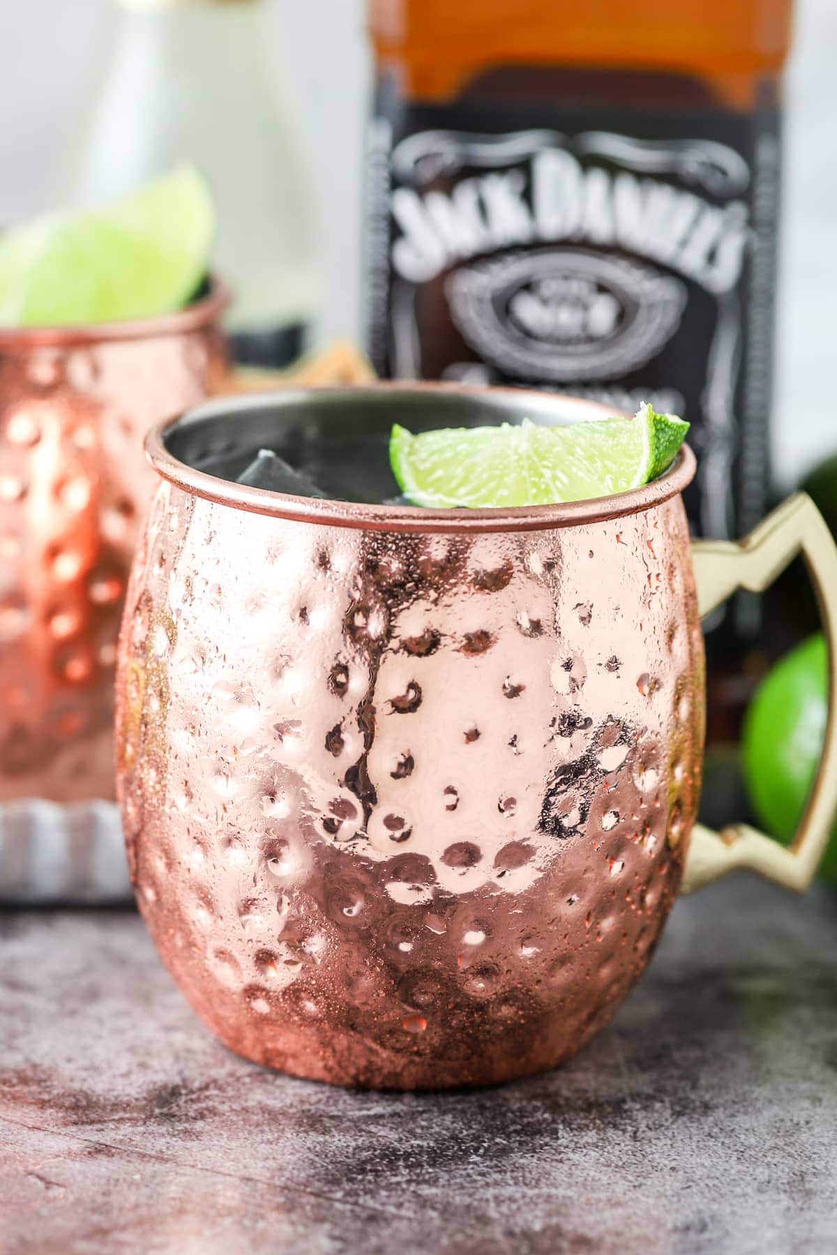 Refreshing tennesse mule with lime and ice in a classic copper mule mug and a bottle of Jack Daniels blurry in the background