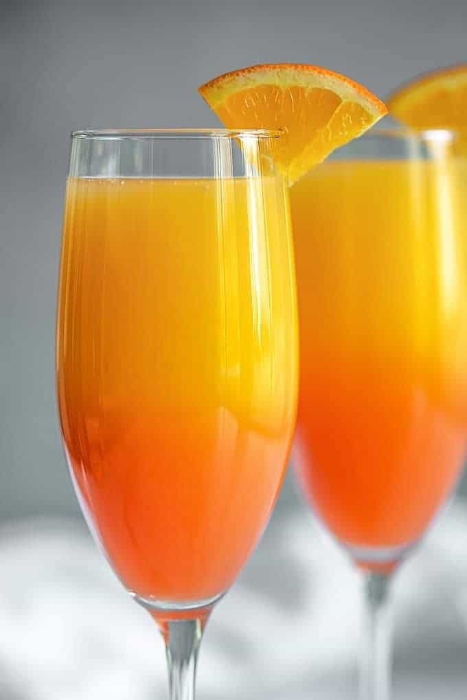 Two glasses of orangey Tequila Sunrise Mimosa with a bottle of champagne.