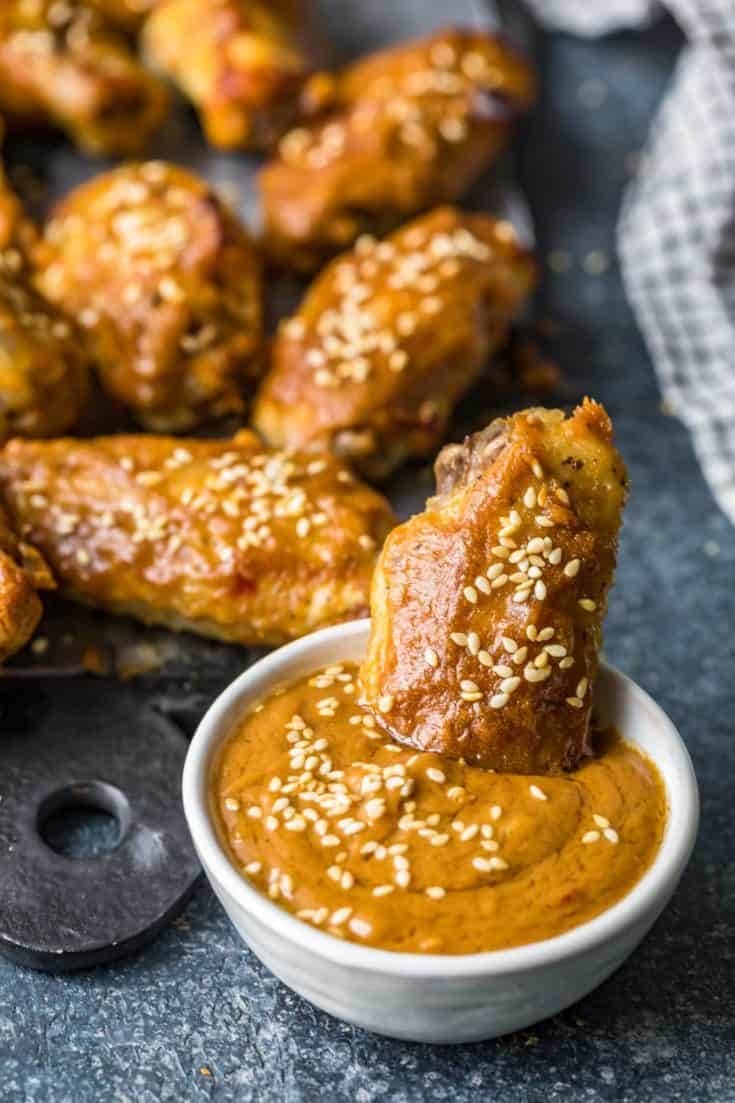 Chicken wings with sesame seeds dipped in a bowl of peanut sauce. 